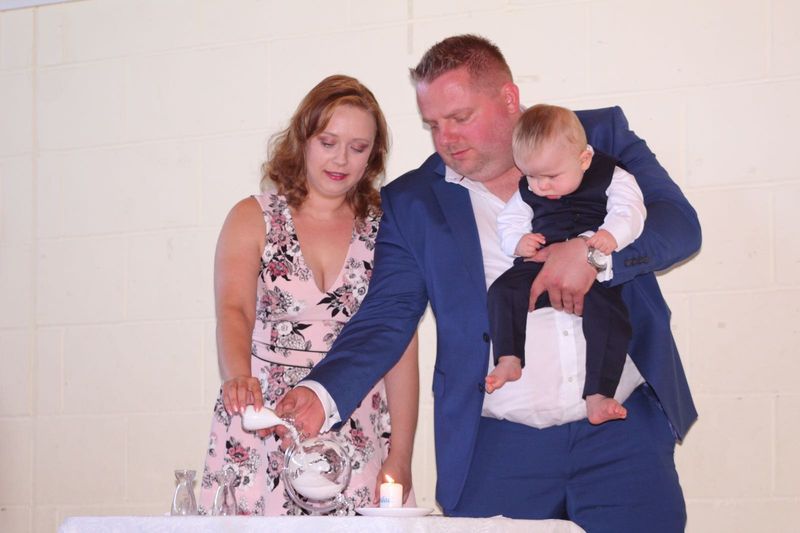 Parents holding their baby son as they pour coloured sand at his naming ceremony