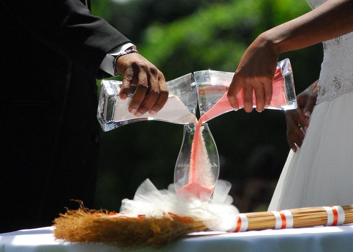 Two hands pouring coloured sand into one glass vase