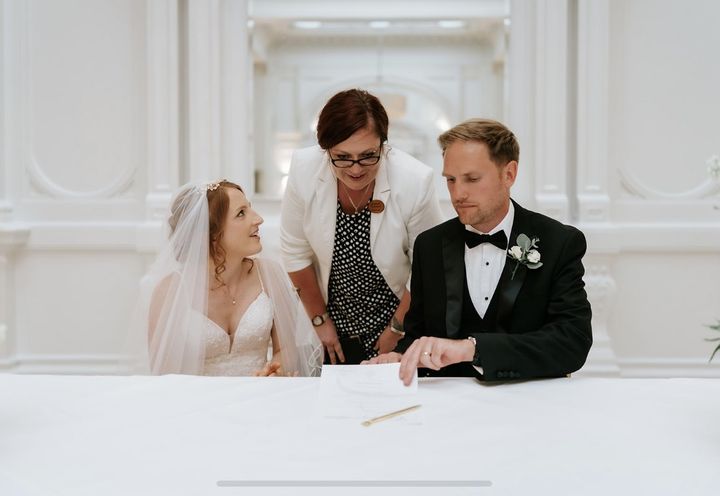 A couple signing their certificate as Roxanne looks on